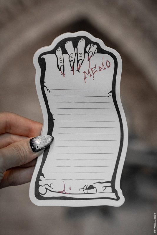 Hand holding a decorative scroll-shaped notepad with a spider design and 'MEMO' text.