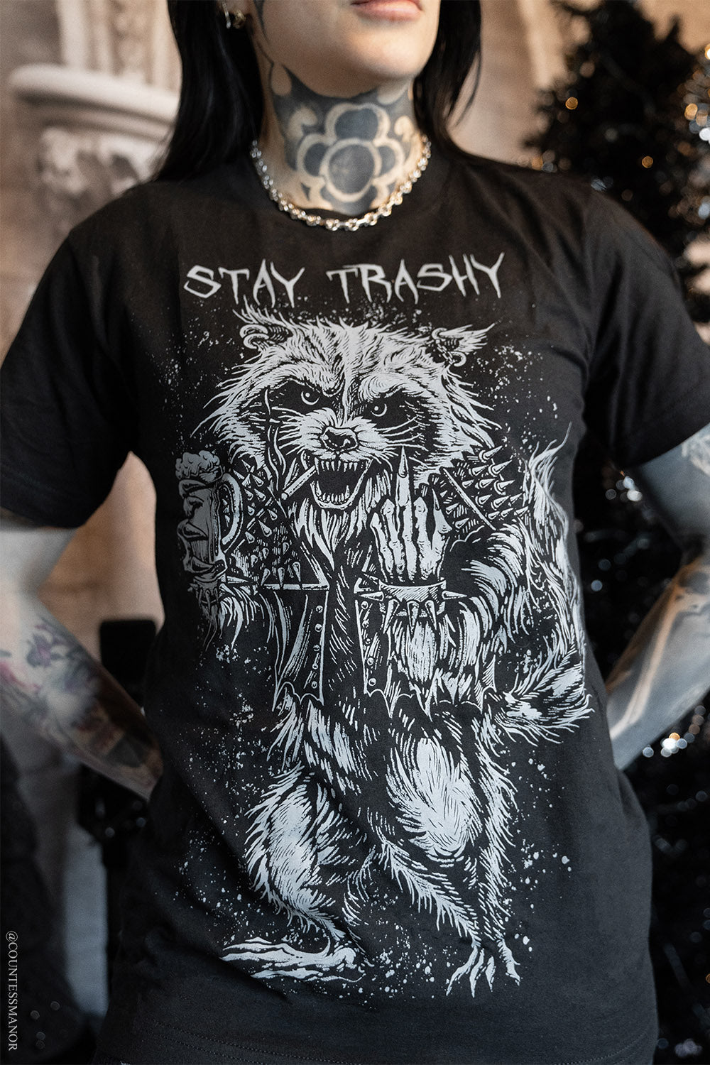 Person wearing a black t-shirt with a graphic design and text 'Stay Trashy' featuring a raccoon