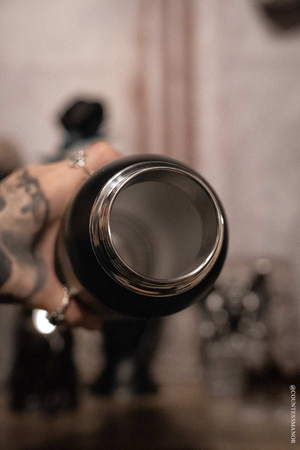 Black thermos held by a hand with tattoos against a blurred background